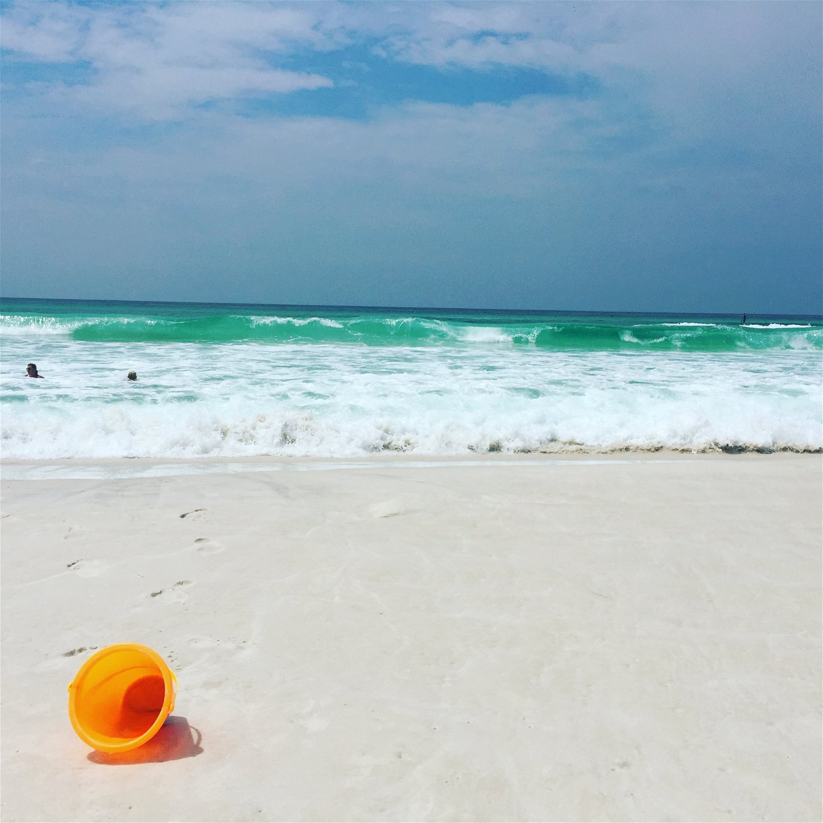 Orange pail on the beach with the ocean and a deep blue sky in the background