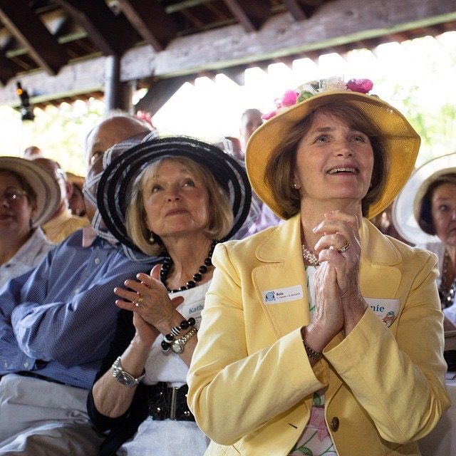 Ladies wearing hats at a horse race and clapping