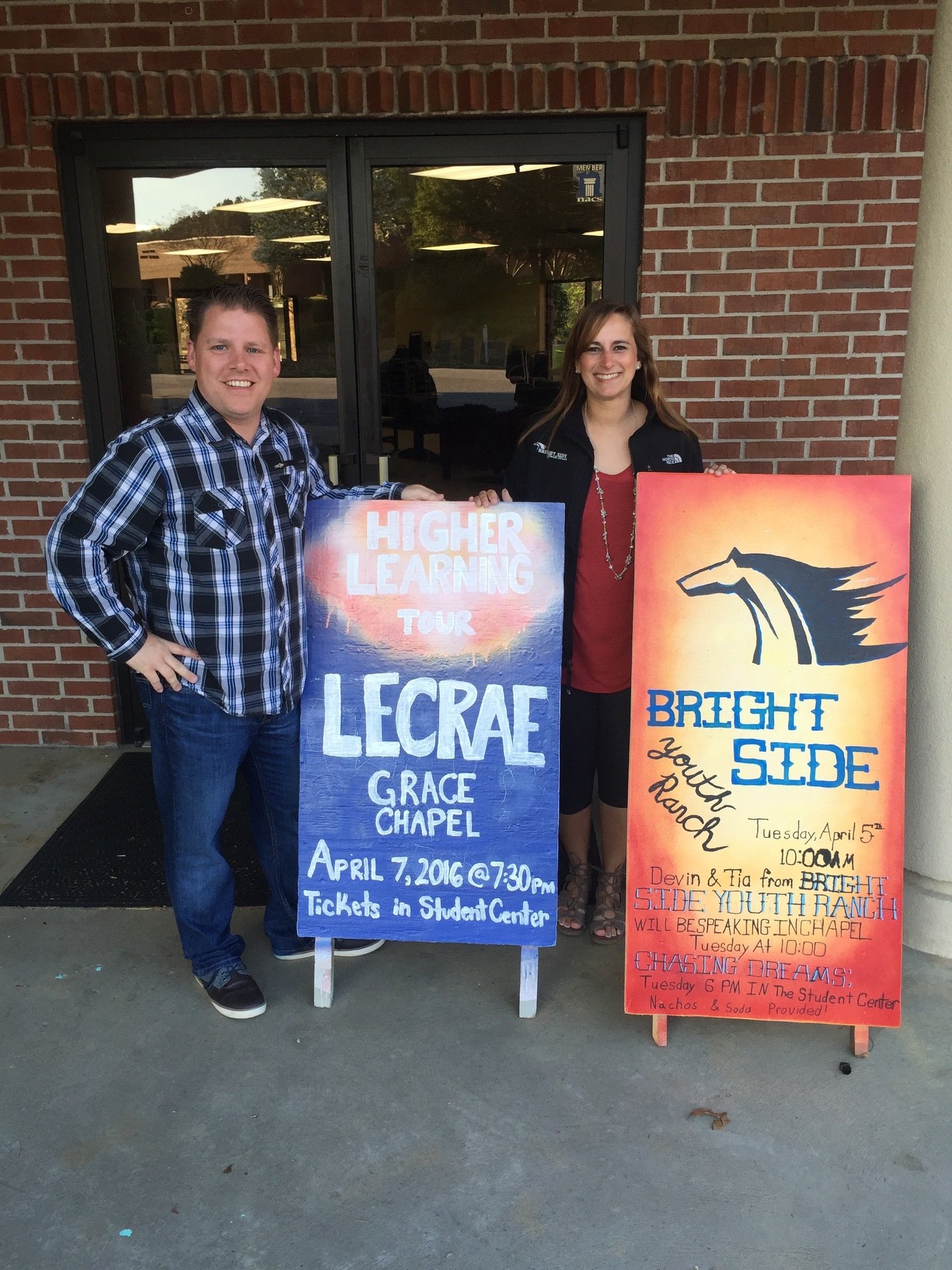 A man and a woman holding signs for Lecrae Grace Chapel and Bright Side Ranch